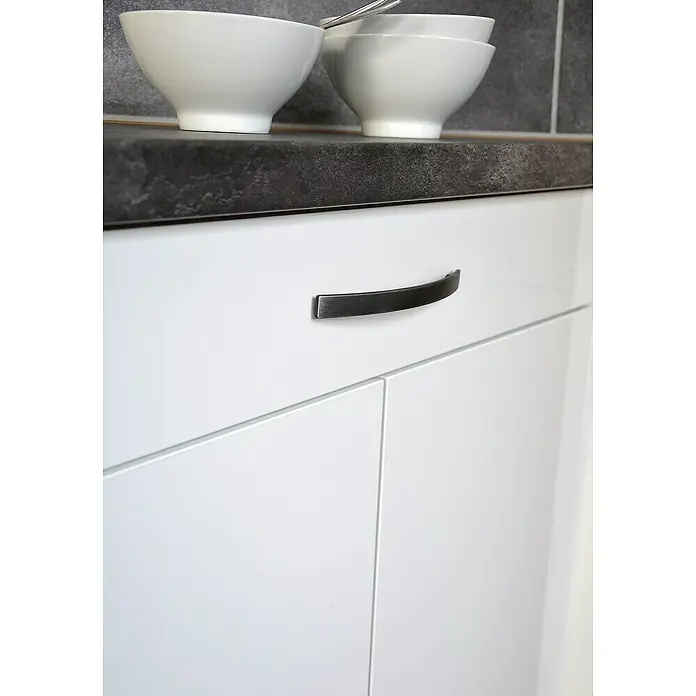 Siro Möbelgriff Möbelgriff 2084 - L x B x H: 15 x 180 x 25 mm, Dunkelgrau, Typ Möbelgriff: Bügel - Detailaufnahme eines weißen Küchenschranks mit einem gebogenen, metallfarbenen Griff und einer dunklen Arbeitsplatte.