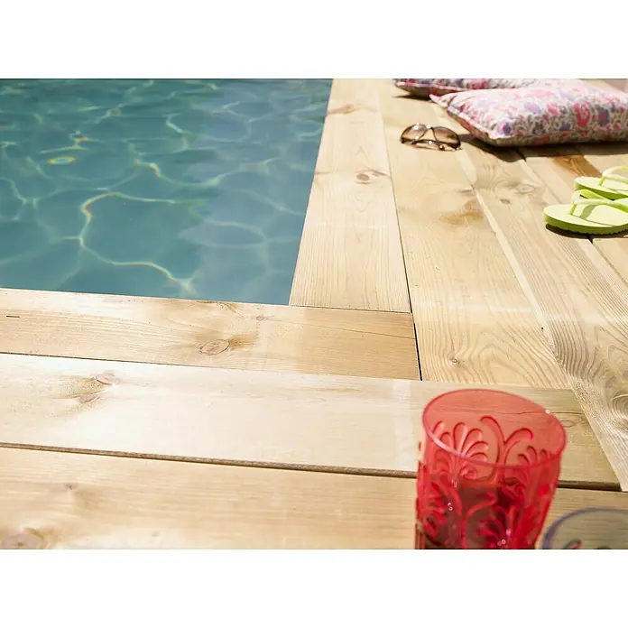 Cerland Tarima para terraza Diego - L x An x Es: 240 x 9,6 x 1,9 cm, Pino - Una bebida refrescante junto a la piscina. El vaso rojo está sobre una cubierta de madera clara, con agua brillante y accesorios relajantes al fondo.
