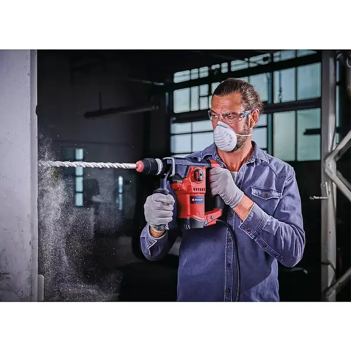 Einhell Martillo combinado TE-RH 32-1600 4F - 1.600 W, 4,5 J, Alojamiento SDS-Plus - El martillo perforador Einhell en acción. Un hombre perfora una pared con gafas de seguridad y máscara.