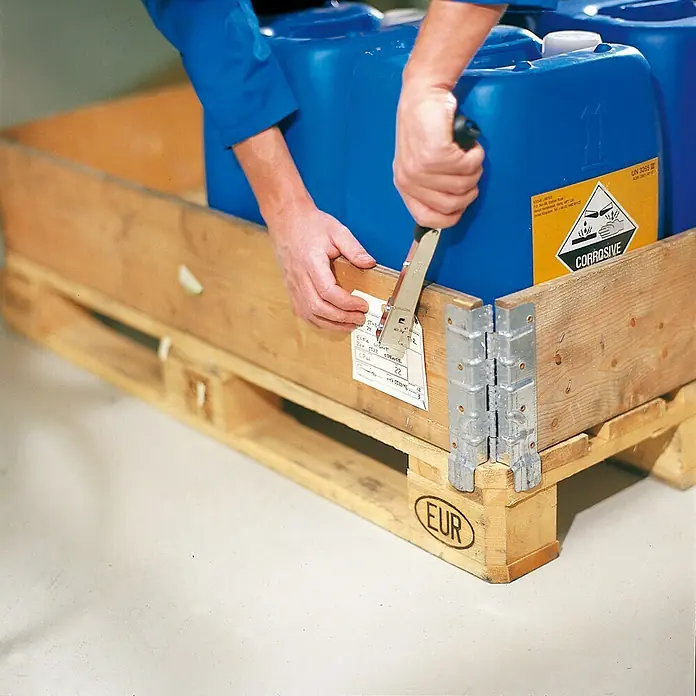 Rapid Hammertacker R19 - Klammertiefe: 4 mm - 6 mm, Geeignet für: Feindrahtklammern Typ 13 (4 - 6 mm), Blisterpack - Eine Person befestigt mit einem Tacker ein Etikett an einer Palette mit blauen Behältern, die mit einem Gefahrgutzeichen versehen sind.