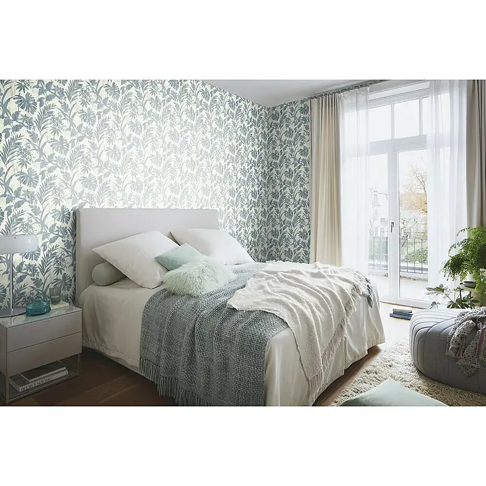 Rasch Vliestapete Beachhouse - Beige/Blau, Floral, 10,05 x 0,53 m - Ein Schlafzimmer mit einem bequemen Bett mit hellgrauer Tagesdecke und Kissen. Die Wand ist mit einer blau-weißen Tapete dekoriert.
