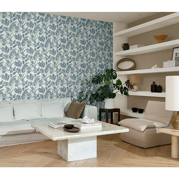 Rasch Vliestapete Beachhouse - Beige/Blau, Floral, 10,05 x 0,53 m - Wohnzimmer mit blau gemusterter Tapete, weißem Sofa, Marmortisch und Regalen, die Dekorationen und Pflanzen enthalten.