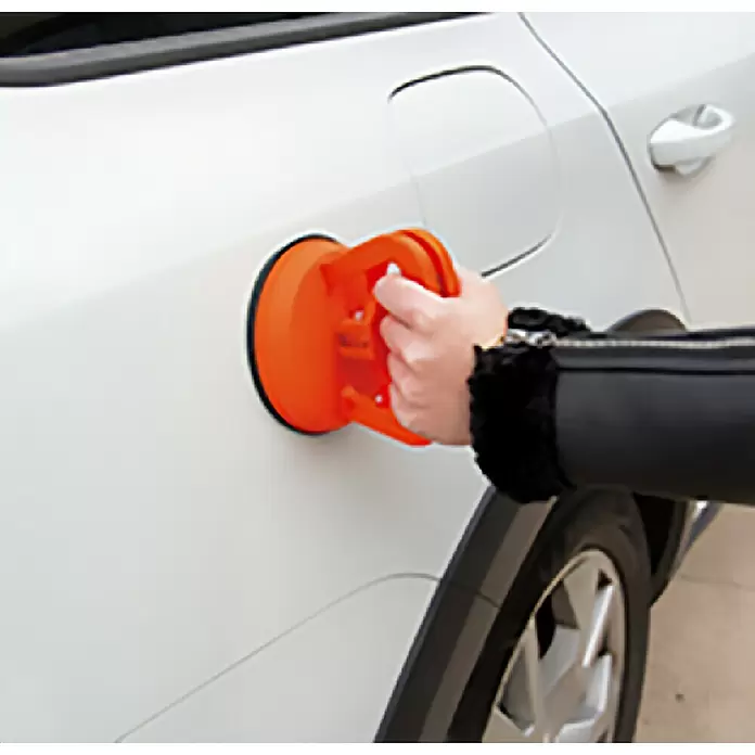 Rolmovil Ventosa - Diámetro: 12 cm, Naranja, Carrocerías - Extractor de abolladuras de ventosa naranja utilizado por una persona para quitar una abolladura de un coche blanco.