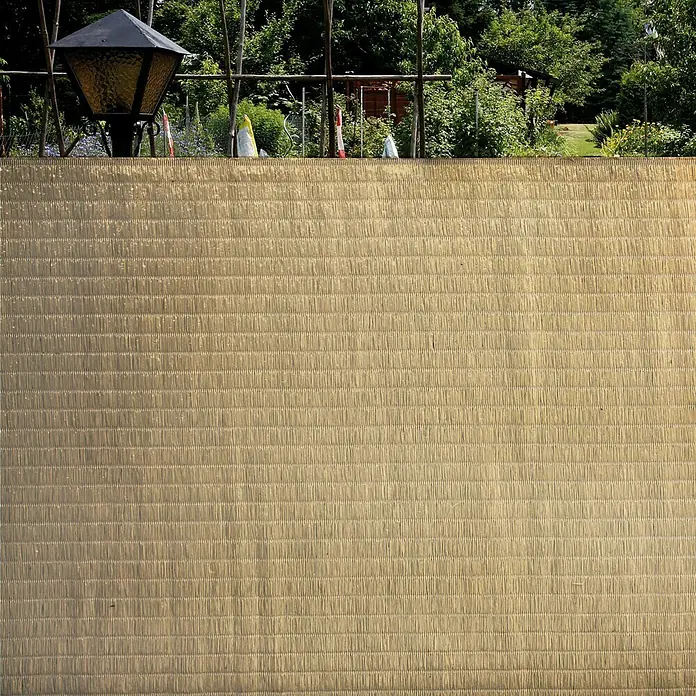 Gardol Balkonsichtschutz Raffia - Beige, 300 x 90 cm - Nahaufnahme einer beigen Sichtschutzmatte im Außenbereich, die Privatsphäre und Windschutz bietet, mit Garten und Laterne im Hintergrund.