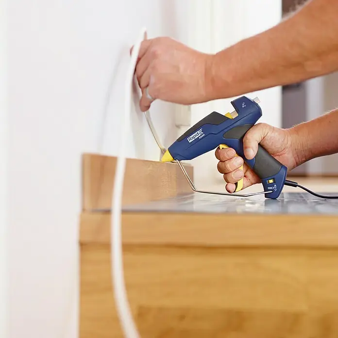 Rapid KlebepatronenGeeignet für: PVC, 12 x 94 mm, Transparent, 125 g - Eine Rapid EG280 Klebepistole wird verwendet, um eine weiße Zierleiste an einer Wand zu befestigen, ideal für DIY-Projekte und schnelle Reparaturen.