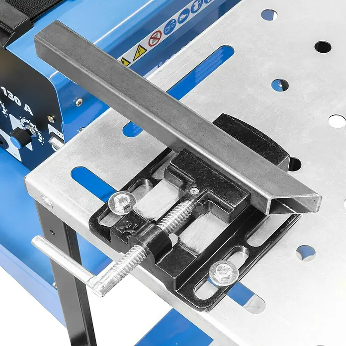 Güde Schweißtisch MST 915 PLUS - L x B: 760 x 500 mm - Das Bild zeigt eine Rohrzwinge, die auf einer Werkbank mit einem Metallstück befestigt ist. Ideal zum sicheren Fixieren von Werkstücken.