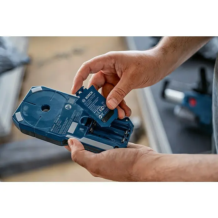 Bosch Professional Ortungsgerät GMS 120-27 - Erfassungstiefe: Max. 120 mm NE-Metalle - Ein Mann legt eine blaue Bosch-Batterie in ein elektronisches Gerät ein.
