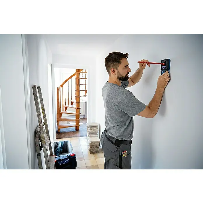 Bosch Professional Ortungsgerät GMS 120-27 - Erfassungstiefe: Max. 120 mm NE-Metalle - Ein Mann benutzt einen Bosch Truvo Leitungssucher, um an einer weißen Wand nach Leitungen zu suchen, wobei er die Position mit einem Bleistift markiert.