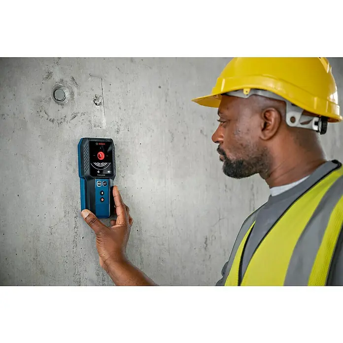 Bosch Professional Ortungsgerät GMS 120-27 - Erfassungstiefe: Max. 120 mm NE-Metalle - Bauarbeiter mit Bosch Ortungsgerät an Betonwand. Das Gerät dient zum Auffinden von Objekten in Wänden vor dem Bohren.
