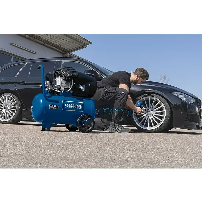 Scheppach Akku-Kompressor AC10/8V - 8 V, 1 Akku, 2 Ah, Max. Druck: 10,3 bar - Ein blauer Scheppach Luftkompressor steht neben einem Mann, der mit einem Schlagschrauber an einem schwarzen Auto arbeitet.