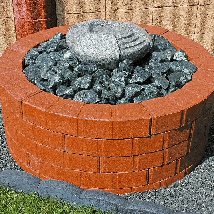 Christoph Randstein Multi- Bord - 50 x 11,5 x 8 cm, Toskana, Beton, Gebogen - Eine kreisförmige Steinbrunnen-Funktion mit einem roten Ziegelgehäuse, gefüllt mit grauen Felsen und einem polierten Steinbrunnenaufsatz.
