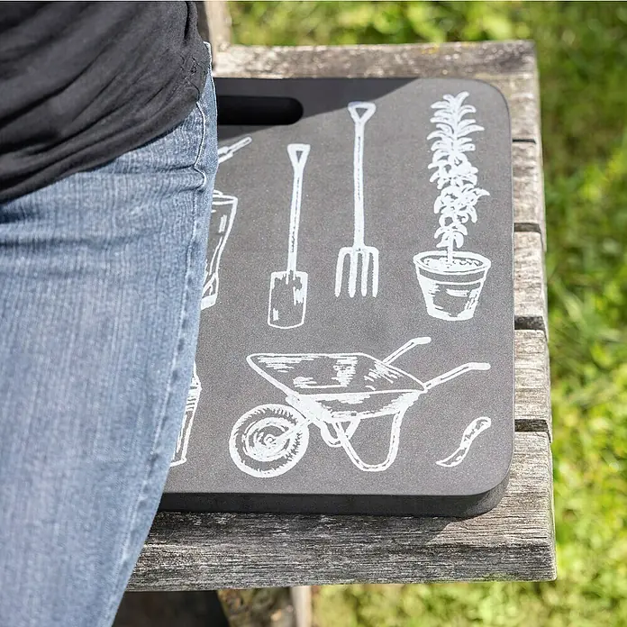 Windhager Motiv Kniekissen - L x B x H: 29 x 39,5 x 2,5 cm - Eine Person sitzt auf einer Gartenbank mit einem grauen Kniekissen, das mit Gartengeräten wie Schaufel und Schubkarre bedruckt ist.