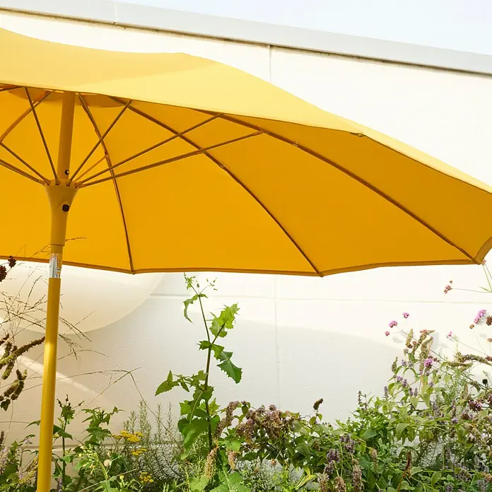 Siena Garden Marktschirm rund Paolo - Curry, Durchmesser Bespannung: 270 cm - Gelber Sonnenschirm spendet Schatten über üppigem Grün.