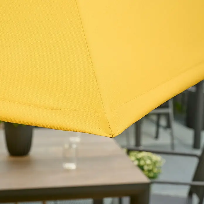 Siena Garden Marktschirm rund Paolo - Curry, Durchmesser Bespannung: 270 cm - Detailaufnahme eines gelben Sonnenschirms, der Schatten auf einen Gartentisch wirft. Perfekt für entspannte Stunden im Freien.