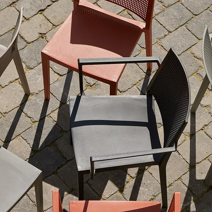 Siena Garden Urban Lights Gartenmöbel-Set Square Sessel/Paco Tisch - Sessel (L x B x H): 56 x 56 x 80 cm, Tisch (L x B x H): 70 x 70 x 71 cm, 3 -tlg., Polypropylen, Melamin, Anthrazit - Mehrere Stühle in verschiedenen Farben stehen auf einem gepflasterten Untergrund, wobei ein schwarzer Stuhl im Zentrum des Bildes steht.
