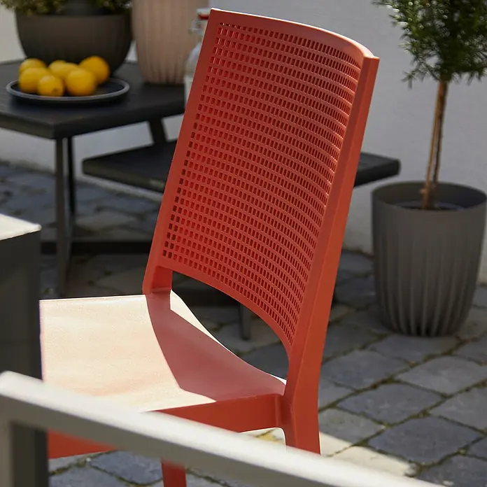 Siena Garden Urban Lights Stapelstuhl Square - Polypropylen, Stapelbar, Brick, B x T x H: 46 x 56 x 80 cm - Nahaufnahme eines orangefarbenen Gartenstuhls mit perforierter Rückenlehne, der auf einer Terrasse im Freien steht.