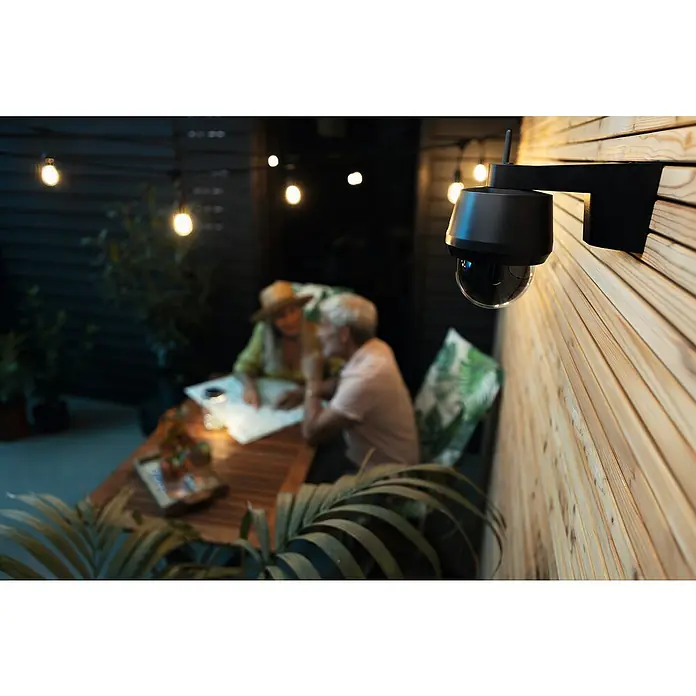 Abus Überwachungskamera-Set Kamera & Monitor Easylook PPDF17100 - Auflösung: 1.024 x 600 Pixel, Schwarz - Eine schwarze Überwachungskamera mit Antenne ist an einer Holzwand montiert, während im Hintergrund ein Paar unter Lichterketten sitzt.