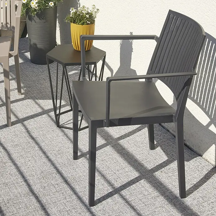 Siena Garden Urban Lights Stapelsessel Lane - Polypropylen, Stapelbar, Anthrazit, B x T x H: 57 x 56 x 80 cm - Nahaufnahme eines anthrazitfarbenen Sessels mit Armlehnen auf einer Terrasse, neben einem Beistelltisch und Blumenkübeln.