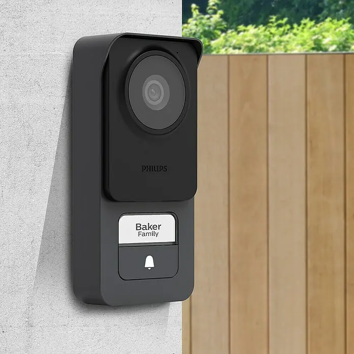 Philips WelcomeEye Türklingel mit Kamera Connect 3 WLAN Komplett-Set - Schwarz - Intelligente Philips-Türklingel mit Kamera und Namensschild "Familie Baker" an einer Wand.