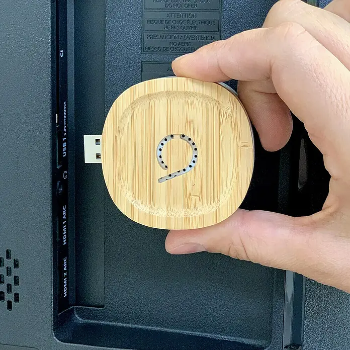 Avidsen Funk-Türgong Drahtlos Bamboo für USB-Anschluss - Grau, Bambus, Reichweite ca.: 100 m - Ein USB-Stick mit einem runden, hölzernen Gehäuse und einem ausgeschnittenen Design wird an einem Fernseher angeschlossen.