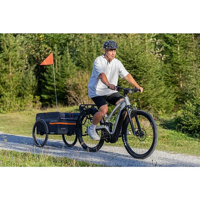 Qeridoo Fahrradanhänger Qubee XL - Max. zulässiges Gesamtgewicht: 60 kg, grau, 220 l - Mann fährt ein E-Bike mit einem Qeridoo-Fahrradanhänger auf einem Waldweg.