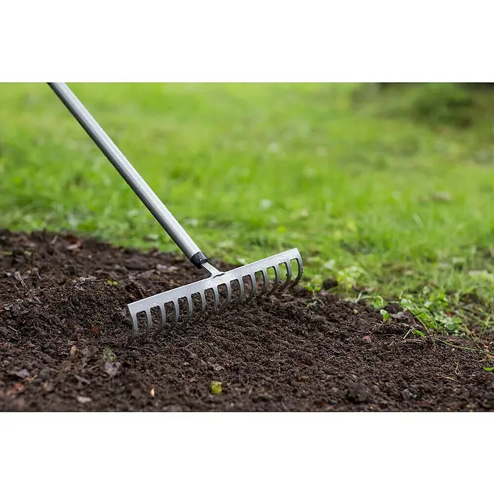 Fiskars Ergonomic Rechen - Aufhängeloch im Griff, Material Gerätekopf: Borstahl - Nahaufnahme eines Metallrechens, der in dunkler Erde liegt, ideal für die Gartenarbeit und die Vorbereitung von Pflanzflächen.