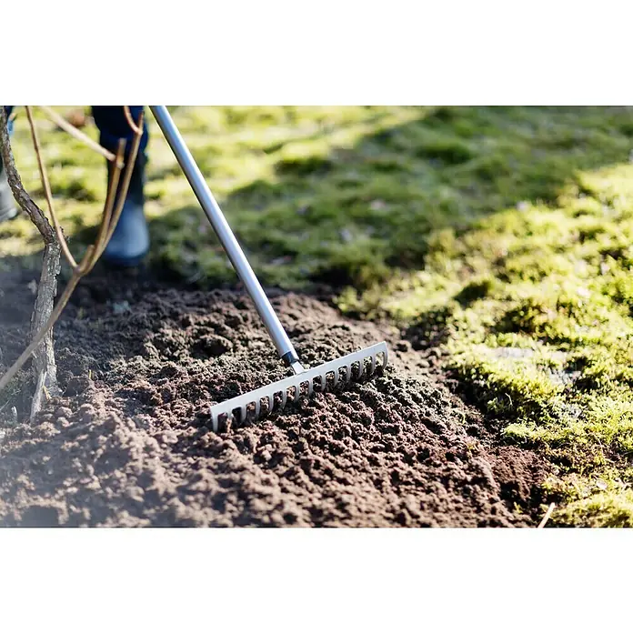 Fiskars Ergonomic Rechen - Aufhängeloch im Griff, Material Gerätekopf: Borstahl - Nahaufnahme einer Harke, die in dunkler Gartenerde liegt, ideal zum Glätten und Vorbereiten von Beeten für die Bepflanzung.