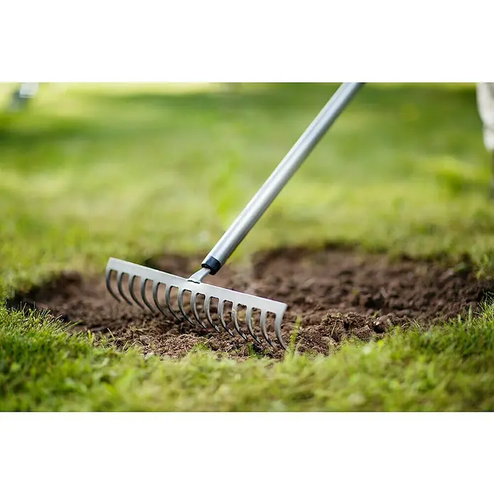 Fiskars Ergonomic Rechen - Aufhängeloch im Griff, Material Gerätekopf: Borstahl - Nahaufnahme eines Metallrechens, der in einem Garten zum Glätten von Erde verwendet wird, um eine ebene Fläche für die Bepflanzung zu schaffen.