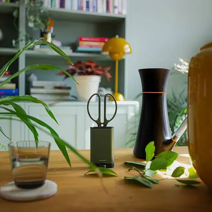 Fiskars Schere - Elegante, freistehende Werkzeughalterung zur praktischen Aufbewahrung, Material Klinge: Stahl, Präzisionsgeschliffen - Ein helles Zimmer mit Gartenschere in Halterung von Fiskars, einer Gießkanne und grünen Pflanzen auf einem Holztisch.