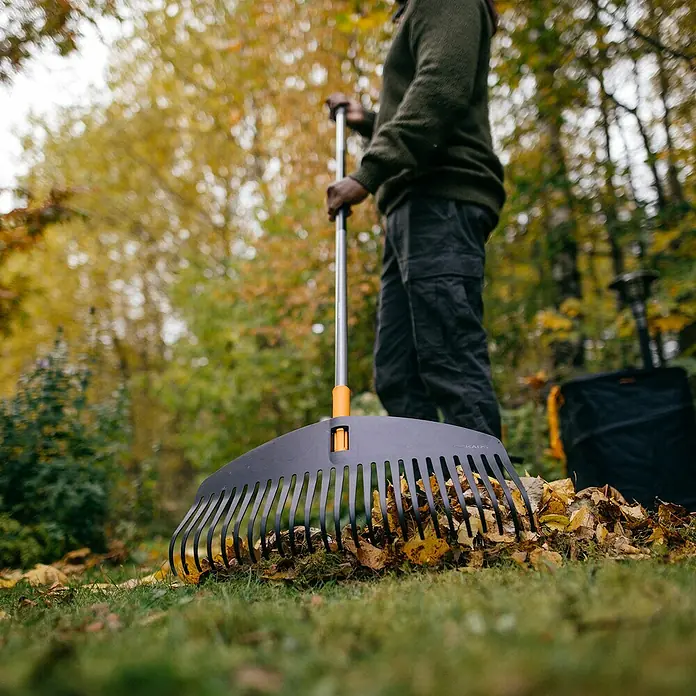 Fiskars Ergonomic Laubbesen - Arbeitsbreite: 51 cm, Ergonomischer Stiel - Nahaufnahme eines Fiskars Laubbesens beim Aufsammeln von Herbstlaub im Garten, ideal für die Gartenarbeit.
