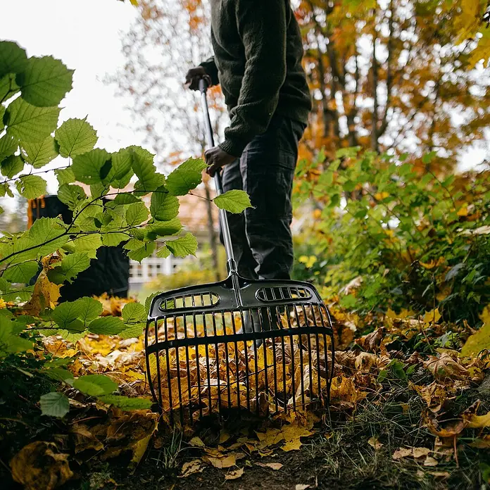 Fiskars Ergonomic Laubschaufel - Material Gerätekopf: Kunststoff, 1 Stk. - Der Laubsammler füllt sich mit bunten Herbstblättern, während eine Person im Hintergrund arbeitet. Ein nützliches Werkzeug für die Gartenarbeit.