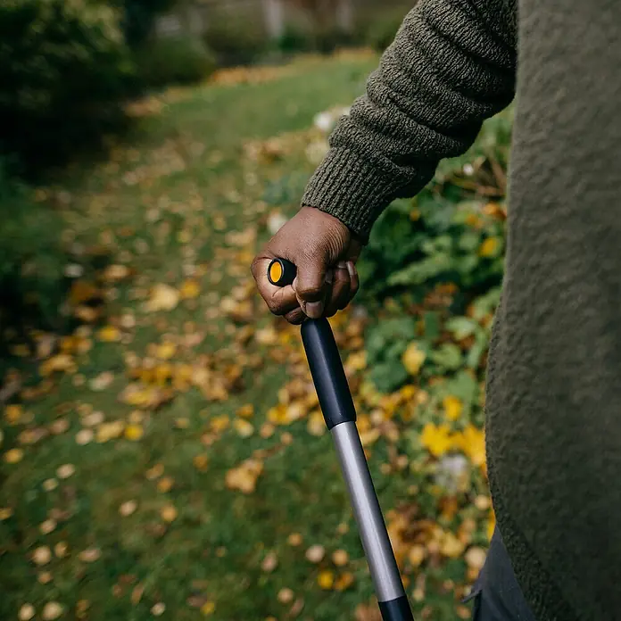 Fiskars Ergonomic Laubschaufel - Material Gerätekopf: Kunststoff, 1 Stk. - Nahaufnahme einer Person, die einen Fiskars-Unkrautstecher mit ergonomischem Griff im Garten hält.