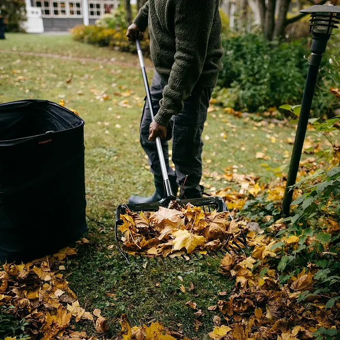 Fiskars Ergonomic Laubschaufel - Material Gerätekopf: Kunststoff, 1 Stk. - Person, die mit einem Fiskars-Laubbesen gelbe Blätter in einen schwarzen Fiskars-Laubsack sammelt.