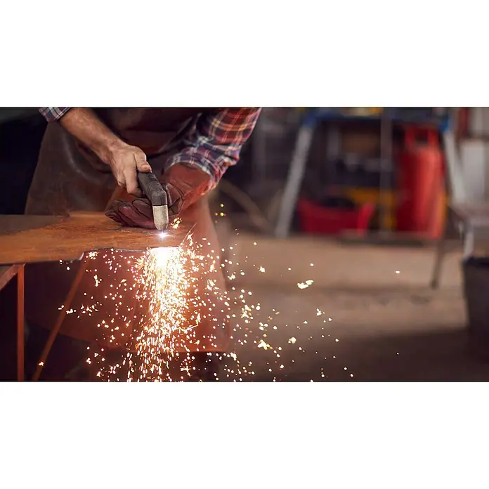 Güde Plasmaschneider GPS-K AIR CUT 40 AK - Schweißstrom: 15 A - 40 A, Max. Schnittstärke: 12 mm, 230 V - Ein Arbeiter mit Schutzhandschuhen und Schürze schneidet mit einem Plasmaschneider ein Metallstück, wobei Funken sprühen.