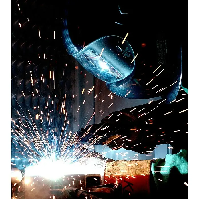 Güde Fülldrahtschweißgerät SG 131 A-SYN - Schweißstrom: 20 A - 120 A, 230 V - Schweißer bei der Arbeit mit Schutzhelm. Funken fliegen, während Metall verbunden wird.