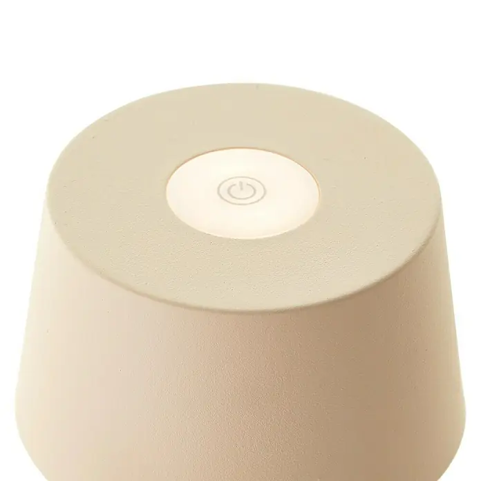Brilliant Akku-Tischleuchte Jona - 2 W, 9 x 25 cm, Beige, Warmweiß - Nahaufnahme einer beigen Tischleuchte mit einem runden, beleuchteten Netzschalter auf der Oberseite vor schwarzem Hintergrund.