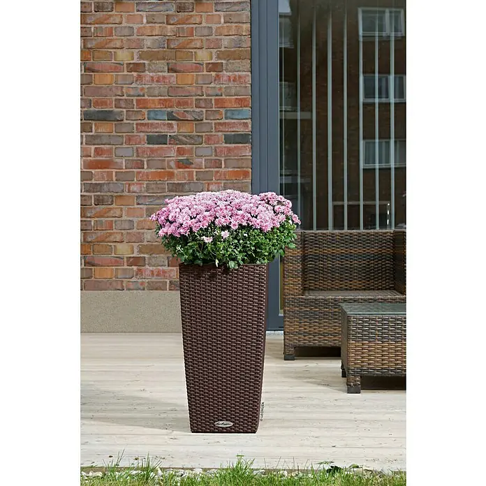 Lechuza Cottage Pflanzsäule eckig Cubico 30 - Außenmaß (L x B x H): 30 x 30 x 56,5 cm, Kunststoff, Mokka - Elegante Nahaufnahme eines hohen, braunen Pflanzgefäßes mit üppigen rosa Blüten, ideal für stilvolle Außenbereiche.