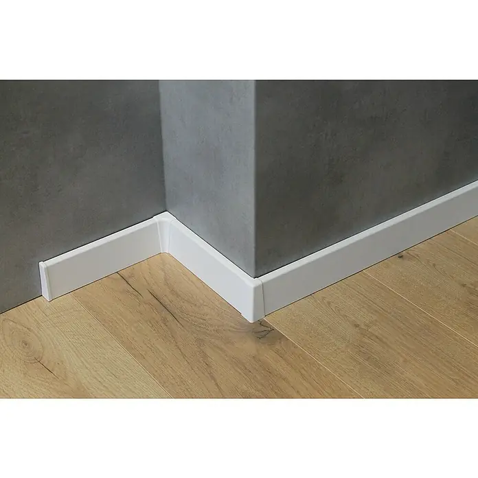 Sockelleiste - 240 cm x 18 mm x 58 mm, MDF, Weiß - Nahaufnahme einer weißen Fußleiste, die auf einem hellen Holzboden an einer grauen Wand entlang verläuft und einen sauberen Übergang schafft.