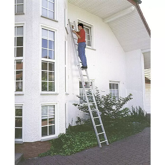 Corda Escalera deslizante - Número de peldaños: 22 ud., Altura de trabajo: 5,3 m, Carga soportada: 150 kg, Aluminio - Escalera extensible de aluminio plateado apoyada en una casa blanca, utilizada para trabajos exteriores.
