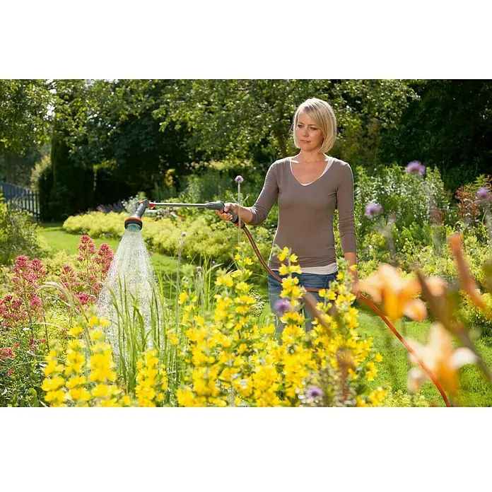 Gardena Comfort Gießstab - 90 cm, Metall/Kunststoff - Eine Frau gießt mit einem Gardena-Gartenschlauch Blumen in einem Garten. Der Schlauch ist orangefarben und hat einen Sprühkopf.