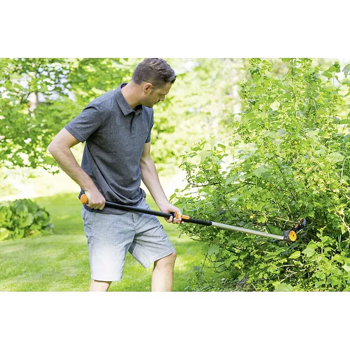Fiskars Schneidgiraffe UPX82 - 166 cm, Max. Aststärke: 32 mm - Ein Mann schneidet Büsche mit einer Fiskars Baumsäge mit Stiel, um das Wachstum zu kontrollieren. Präzise und komfortable Gartenarbeit leicht gemacht.