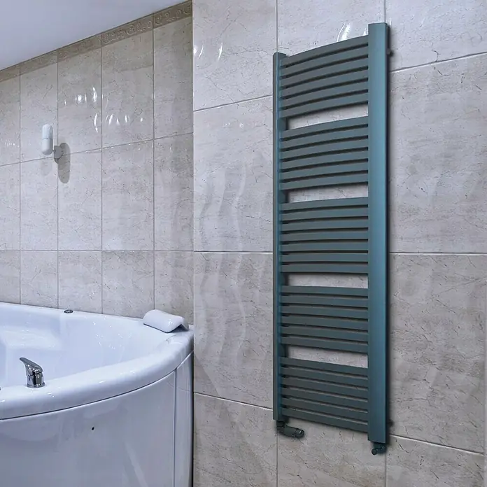 Camargue Badheizkörper Kastor - B x H: 580 x 1.600 mm, Wärmeleistung bei Vorlauftemperatur von 75 °C (D: 50): 1.103 W, Graphit - Handtuchwärmer in Grau an einer gefliesten Badezimmerwand neben einer Badewanne, der für warme Handtücher und ein behagliches Badezimmer sorgt.