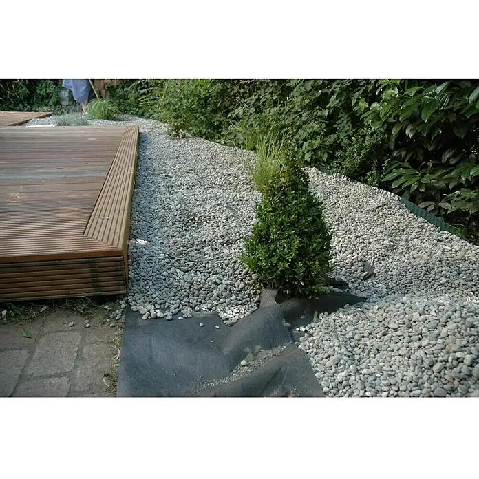 Terrassenvlies Meterware - 100 cm, Grau, 80 g/m² - Gartenweg mit grauen Kieselsteinen und einem kleinen, grünen Busch. Die Steine liegen auf einem schwarzen Untergrund.