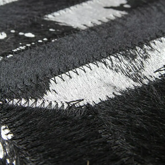 Kayoom Lederteppich DazzleSchwarz/Silber, 150 x 80 cm, 100 % Leder - Detailaufnahme eines schwarz-silbernen Patchwork-Teppichs aus Kuhfell, der durch seine markanten Nähte und das luxuriöse Material besticht.