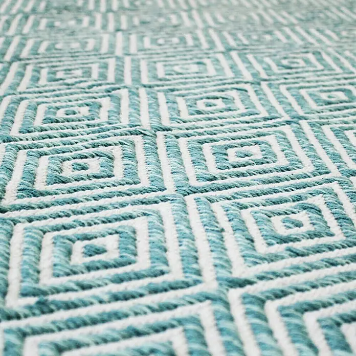 Kayoom Flachgewebeteppich Cocktail 300 - Türkis, 150 x 80 cm, 100% Baumwolle - Nahaufnahme eines stilvollen Teppichs mit einem geometrischen Muster in Türkis und Weiß. Der Teppich verleiht jedem Raum eine moderne Note.