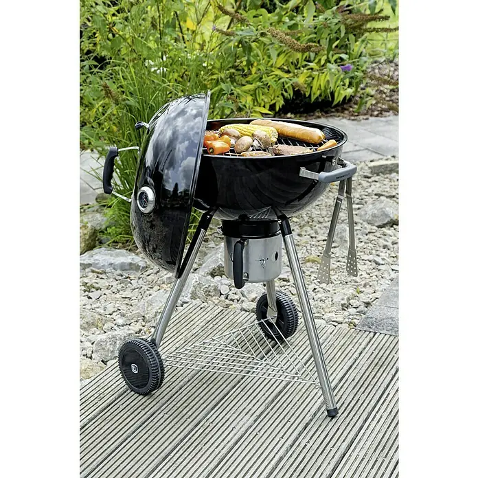 Kingstone Barbacoa redonda con tapa Bullet 57 - Diámetro de la superficie de la parrilla: 57 cm, Negro - Primer plano de una parrilla esférica negra con alimentos como salchichas, verduras y mazorcas de maíz en el jardín.