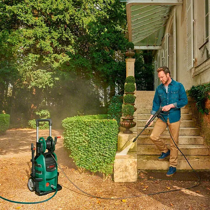Bosch Hochdruckreiniger AdvancedAquatak 150 - 2.200 W - Ein Mann benutzt einen grünen Bosch Hochdruckreiniger im Freien, um eine Steintreppe zu säubern. Ideal für Gartenarbeiten und Reinigungsarbeiten.