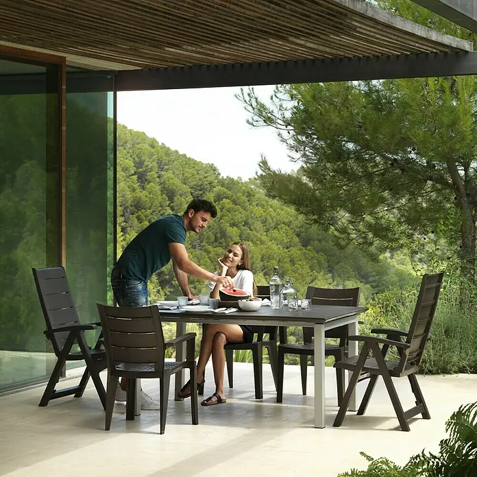 Sillón de posiciones Legno - 65 x 63 x 108 cm, Marrón, Polipropileno, Respaldo regulable - Un conjunto de mesa de comedor con sillas a juego se encuentra en un patio, perfecto para comidas al aire libre.