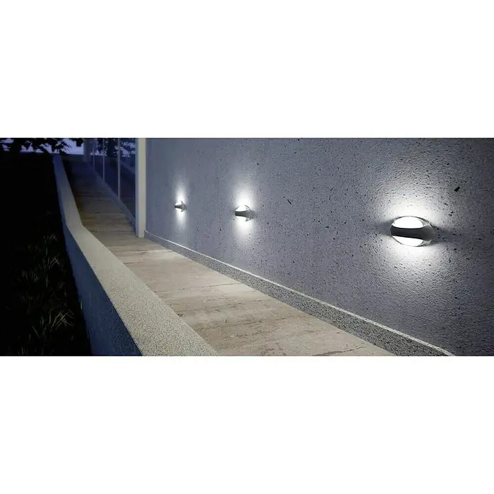 Lutec Aplique exterior LED Eyes - 8,5 W, 7,3 x 18,4 x 11,5 cm, Antracita/Blanco, IP54 - Lámparas de pared modernas iluminan un camino gris a lo largo de una pared, creando una iluminación exterior elegante.