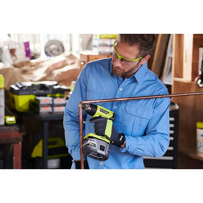 Ryobi ONE+ Akku-Heißluftgebläse R18HG-0 - 0 °C - 470 °C, Ohne Akku - Ein Mann benutzt eine Ryobi Akku-Heißluftpistole zum Löten von Kupferrohren in einer Werkstatt.